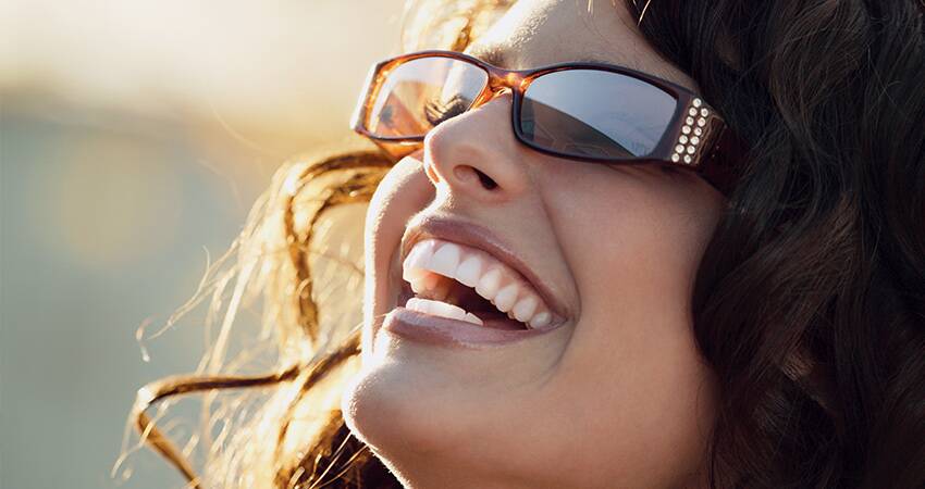 A woman laughing while wearing sunglasses, looking up toward the bright sun