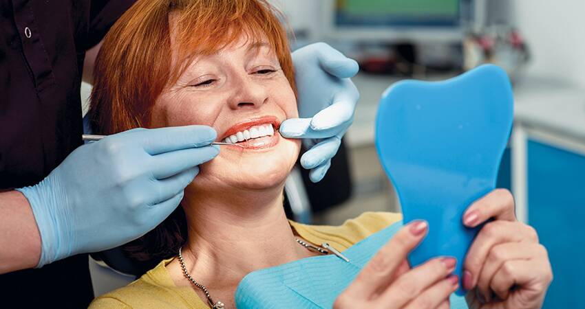 a woman in the dentist chair looking into a mirror and smiling widely